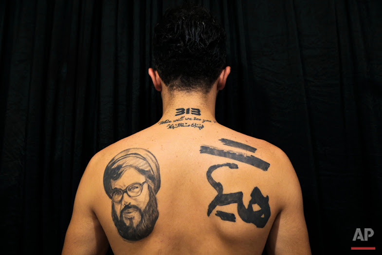 In this Tuesday, July 19, 2016 photo, Hamza, 25, poses for a photo showing off his tattoos of Hezbollah leader Hassan Nasrallah and Shiite Muslim religious slogans in the southern suburb of Beirut. The tattoo in Arabic reads, "It is impossible to humiliate us." (AP Photo/Hassan Ammar)
