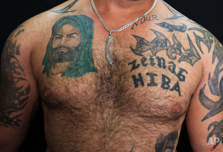 In this Tuesday, July 19, 2016 photo, Zulfiqar, 30, poses for a photo showing his tattoo of Shiite Muslims' first Imam Ali, left, in the southern suburb of Beirut. (AP Photo/Hassan Ammar)